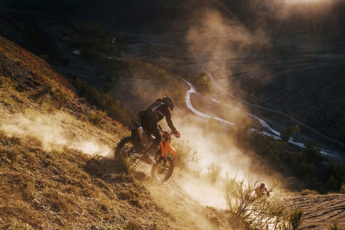 Biker Driving Downhill at sunset off road with dust and watered terrain.