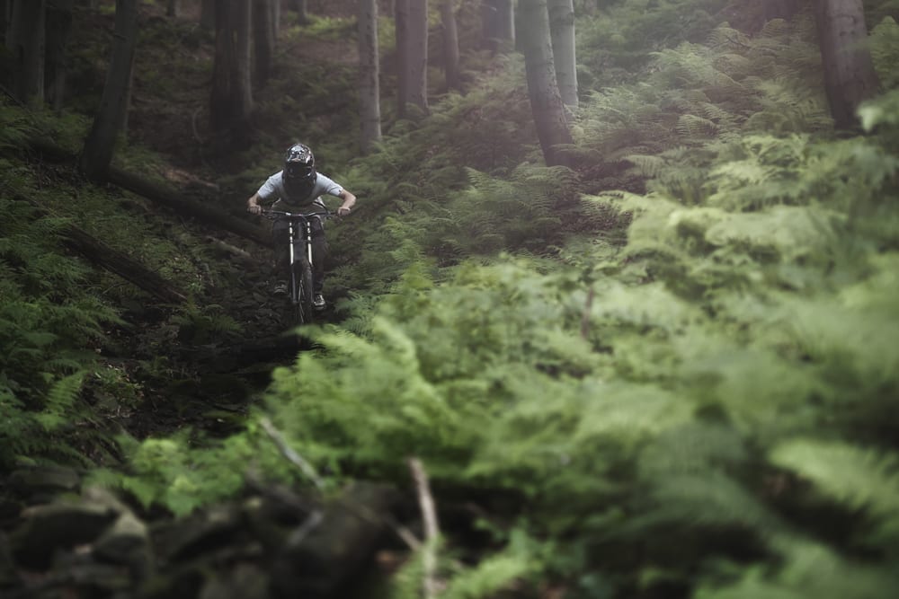 Motorcyclist Driving through Forest. Off-Road wet terrain with green forestry.