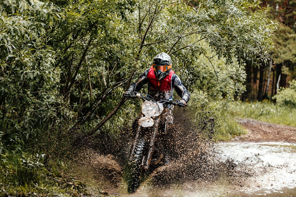 Enduro athlete on motorcycle crosses a puddle of water and mud racing motocross